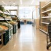Early-morning Japanese chain-store aisle with baskets, produce crates and quiet retail lighting, without logos or readable text.