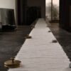 A long strip of handmade paper is held across a stone table by brass weights and small stones.