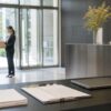 Quiet office lobby with a courier handoff, blank paperwork and a closed laptop on an unbranded service desk.