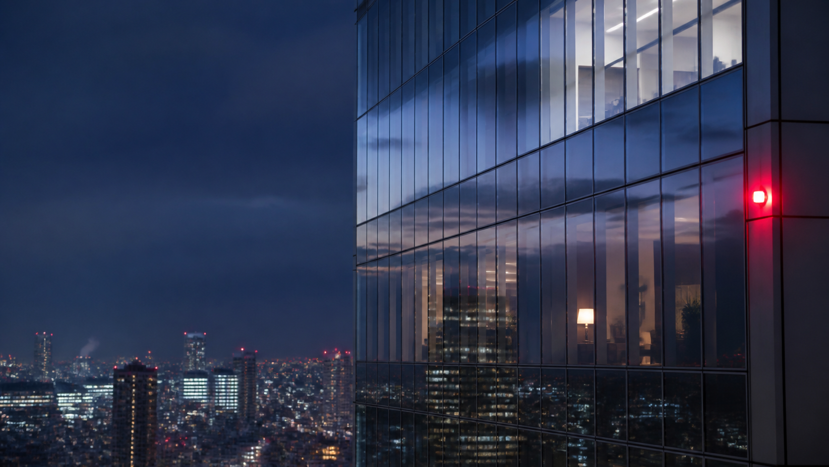 Glass high-rise at blue hour with reflected city lights and a single red aviation light