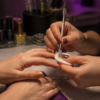 A nail technician removes metallic-gold polish from a client's fingernails at an unbranded salon table.