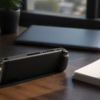 An unbranded handheld game console rests on a quiet desk beside a closed laptop and blank papers.