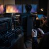 Unbranded game QA room with device racks, testers using controllers and abstract monitor light.
