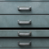 Four blank steel archive drawers with one compartment slightly open in a worn records cabinet.