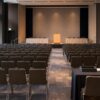 Empty conference hall prepared for a Japanese shareholder meeting with an unbranded stage and rows of seats.