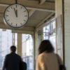 Analog platform clock above morning commuters at an unbranded urban rail station.
