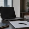 Currency research desk with blank papers, a laptop angled away and soft daylight.