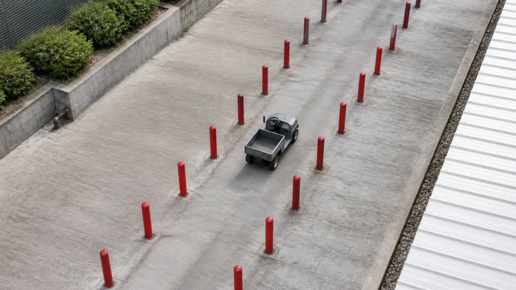 Small unbranded utility cart moving between two rows of red bollards on a plain concrete lane.