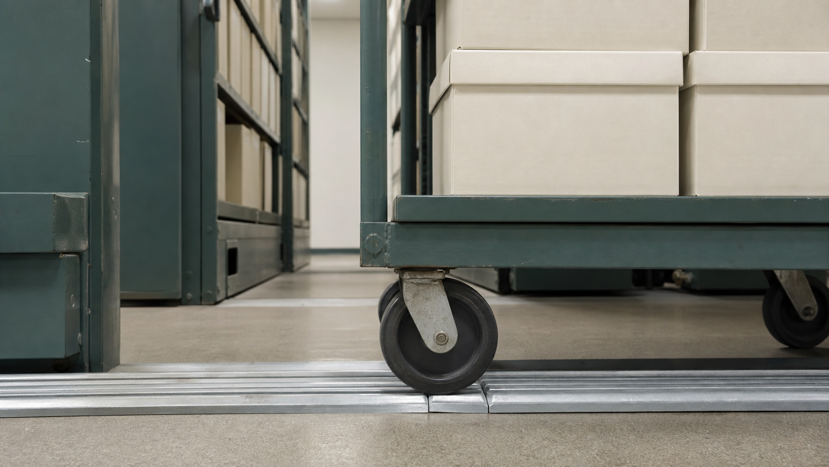 An archival retrieval cart crosses metal floor rails between compact shelves.