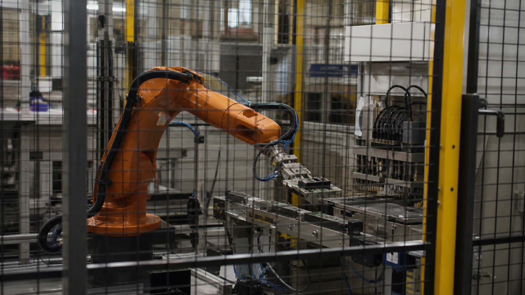 A compact industrial robot works inside a fenced electronics test cell.