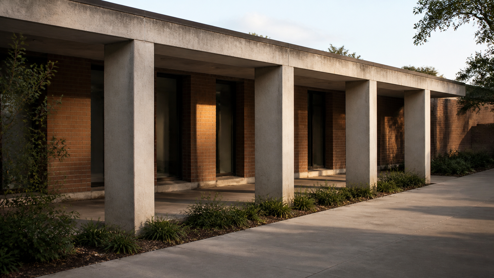 Four concrete bays recede along a brick office courtyard in late-afternoon light.