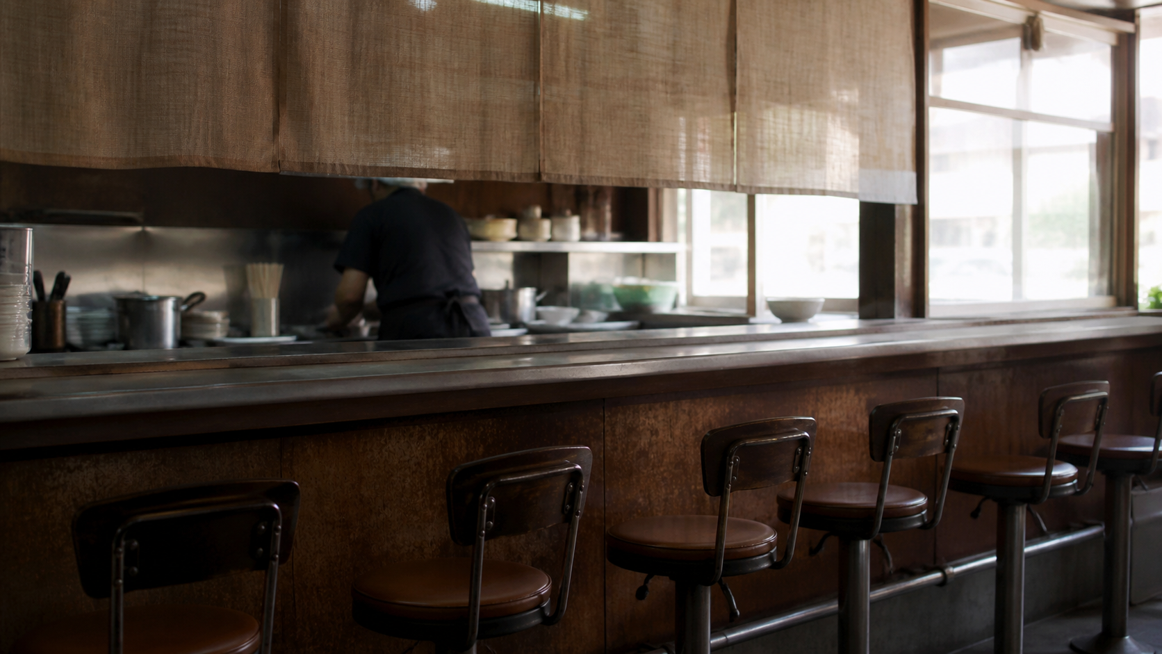 Quiet unbranded lunch counter with empty stools and a worker between services.