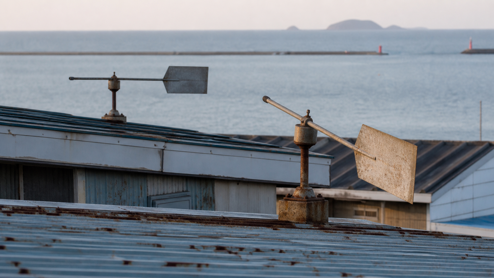 Two plain metal wind vanes on neighboring harbor roofs point along visibly different axes.