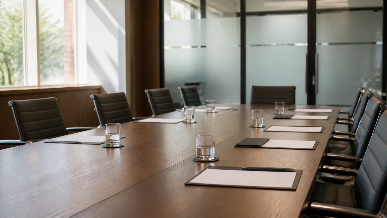 Empty modern boardroom table with blank papers and soft daylight, no logos or readable text.