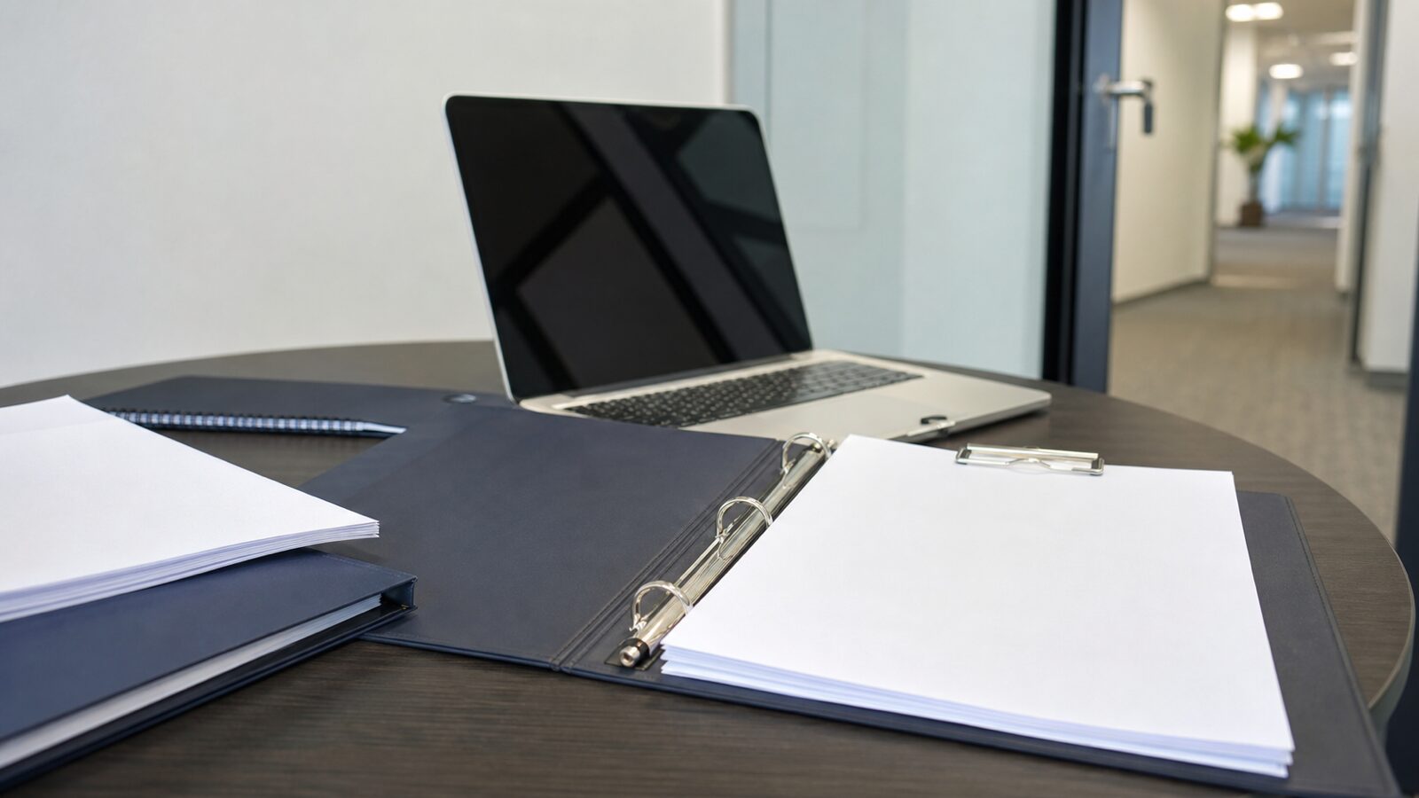 An open binder with blank pages and a laptop on a small office conference table