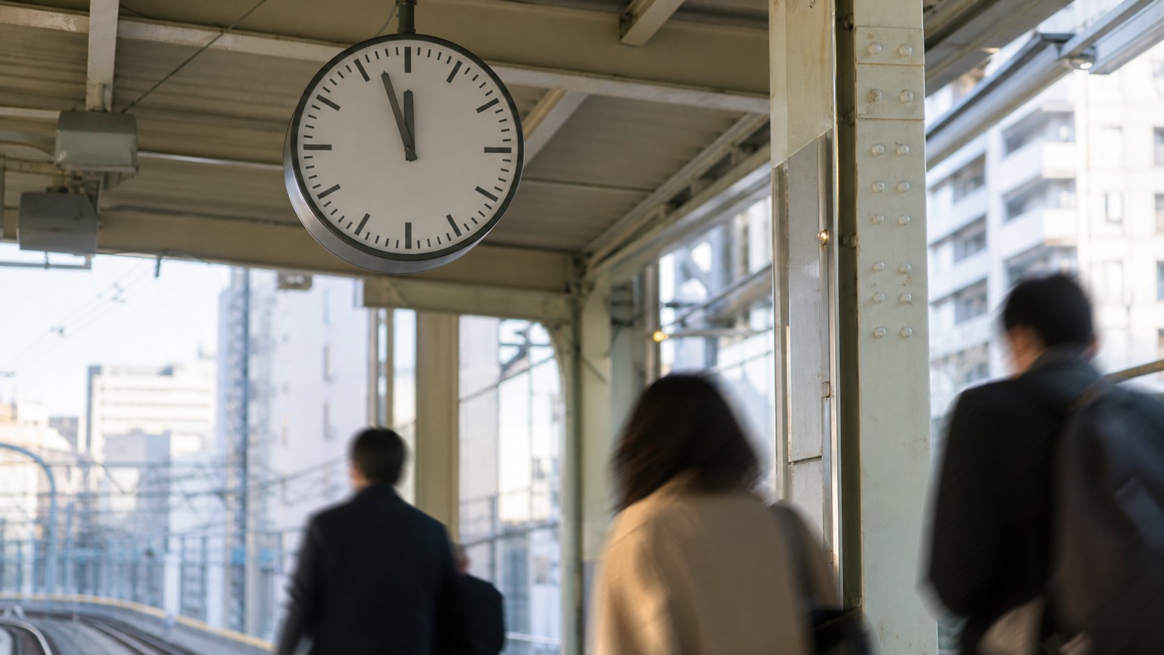 Analog platform clock above morning commuters at an unbranded urban rail station.