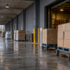 Anonymous bulk-goods pallets on wheeled dollies beneath a rain-damp warehouse loading canopy