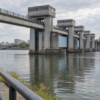 An unbranded concrete floodgate bridge spans a calm urban canal under overcast skies.