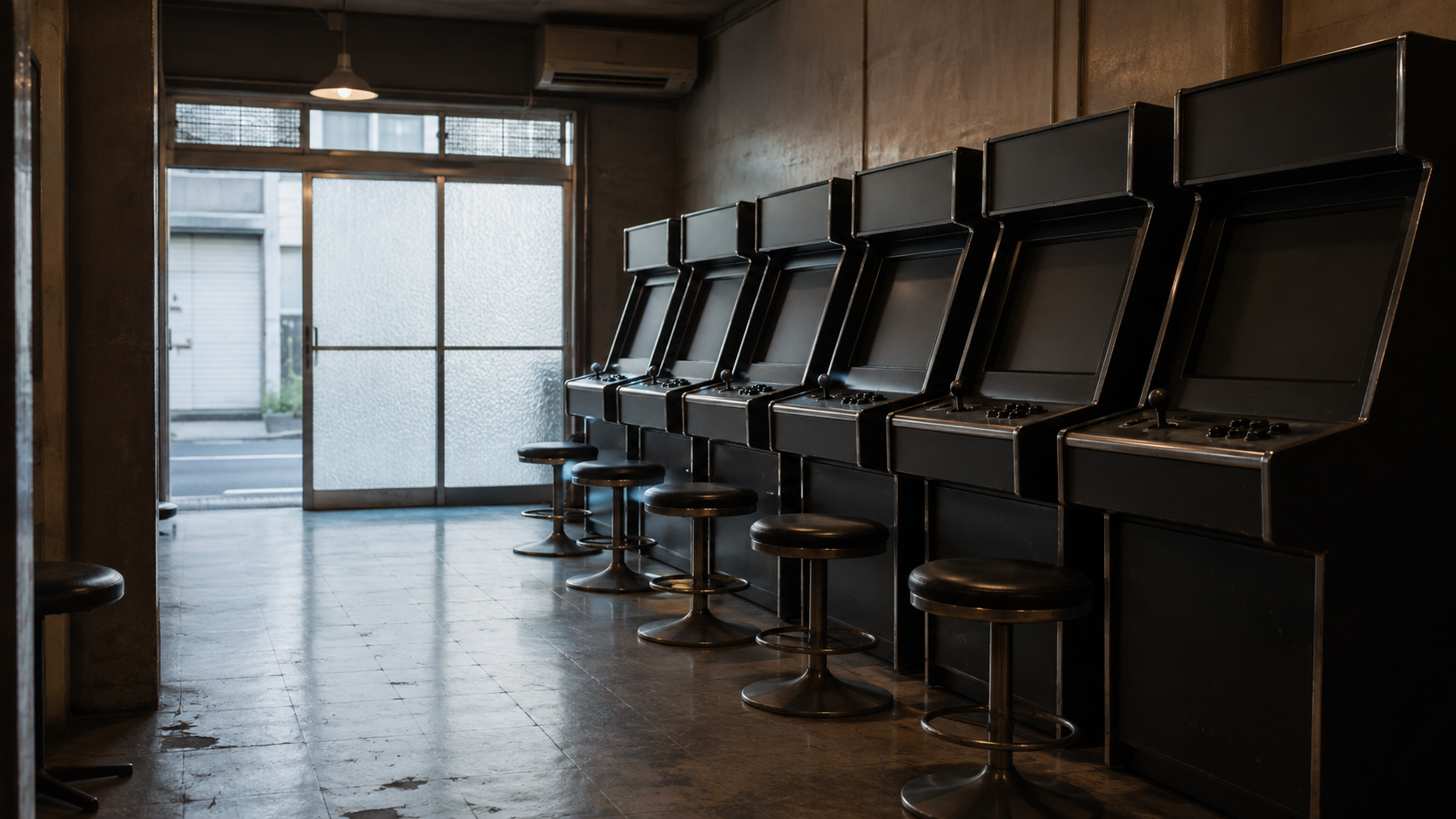 An unbranded arcade interior before opening, with a row of dark cabinets and empty stools.