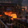 A glowing steel coil moves through an unbranded hot-strip rolling mill at pre-dawn.