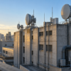 Unbranded microwave relay antennas stand above a weathered urban telecommunications exchange at sunrise.