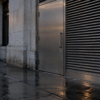 A brushed-steel service door and louvered grille sit in an unbranded limestone building above rain-wet pavement.