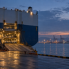 An unbranded vehicle carrier at a dawn harbor, with plain cars visible inside its open stern.