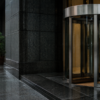 Rain-dark granite and an unbranded stainless-steel revolving door at a Tokyo financial-district bank entrance