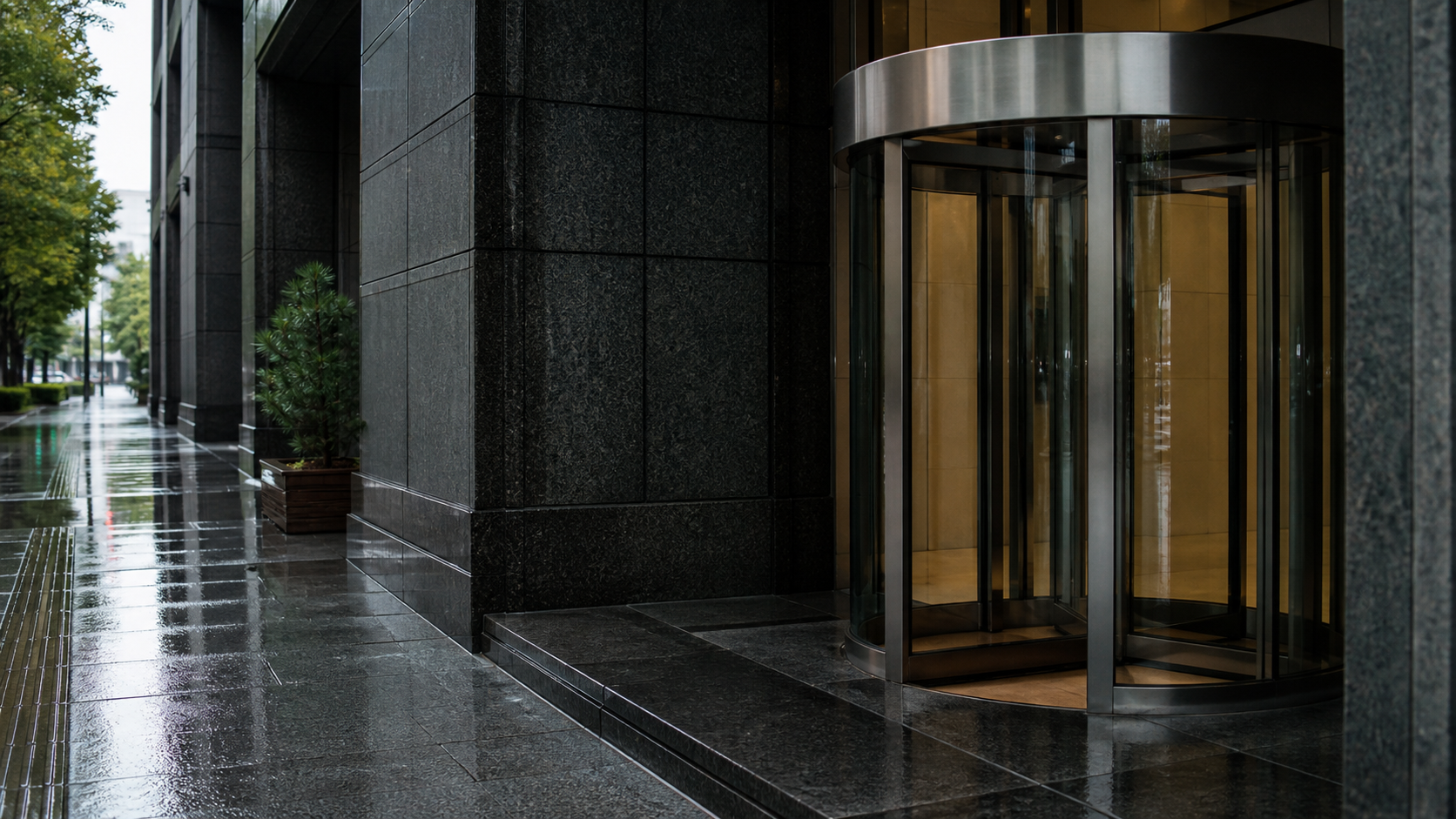 Rain-dark granite and an unbranded stainless-steel revolving door at a Tokyo financial-district bank entrance