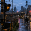 An unbranded amber railway signal beside a rain-wet city street at blue hour, with a cyclist passing in the background.