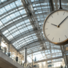 An unbranded analog clock hangs beneath a glass-and-steel urban transit canopy.