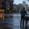 An unbranded bicycle courier walks through a rain-washed city intersection at dawn.
