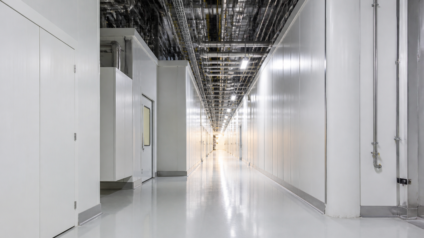 Empty unbranded semiconductor cleanroom service corridor with white panels and overhead stainless pipes