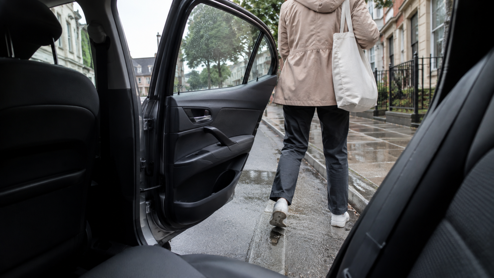 A passenger with a plain tote bag steps from an unbranded car onto a wet curb.