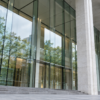 A quiet modern public building entrance with pale stone columns and layered glass reflections.