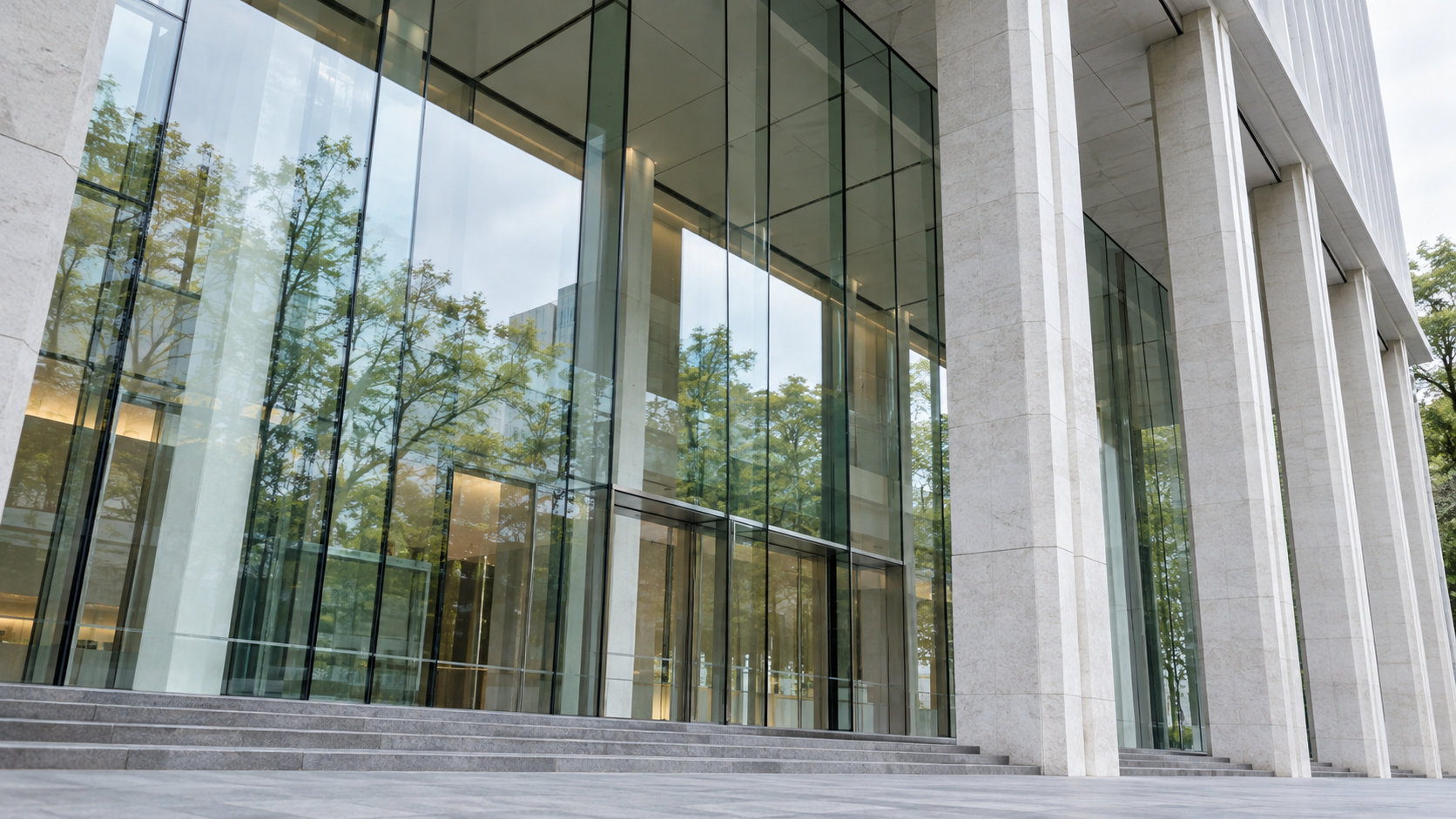 A quiet modern public building entrance with pale stone columns and layered glass reflections.