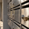 A brass key rests in an unbranded brushed-metal apartment mailbox lock in warm daylight.