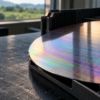 A polished silicon wafer in an unbranded graphite carrier on a dark industrial inspection surface.