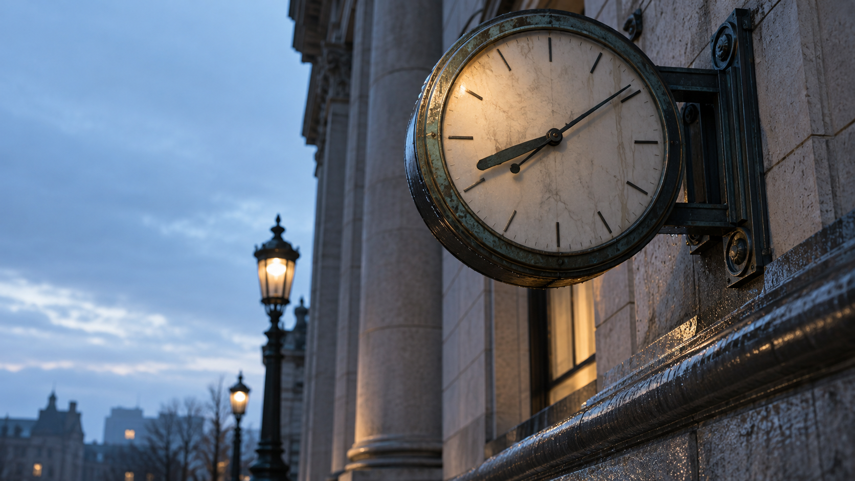 An unnumbered analog clock is mounted on a weathered stone building wall at blue hour.
