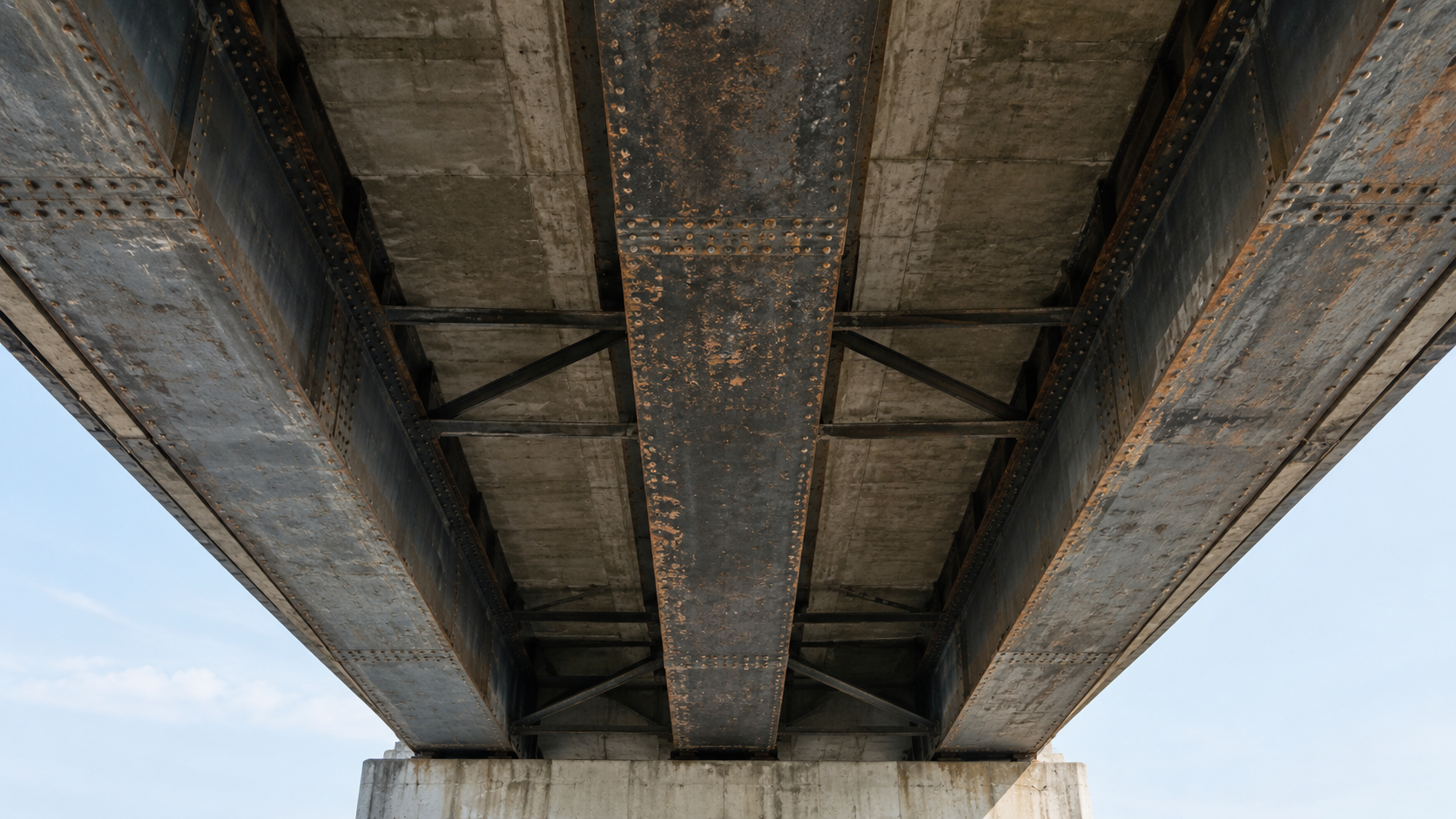 Weathered steel support beams beneath an urban footbridge