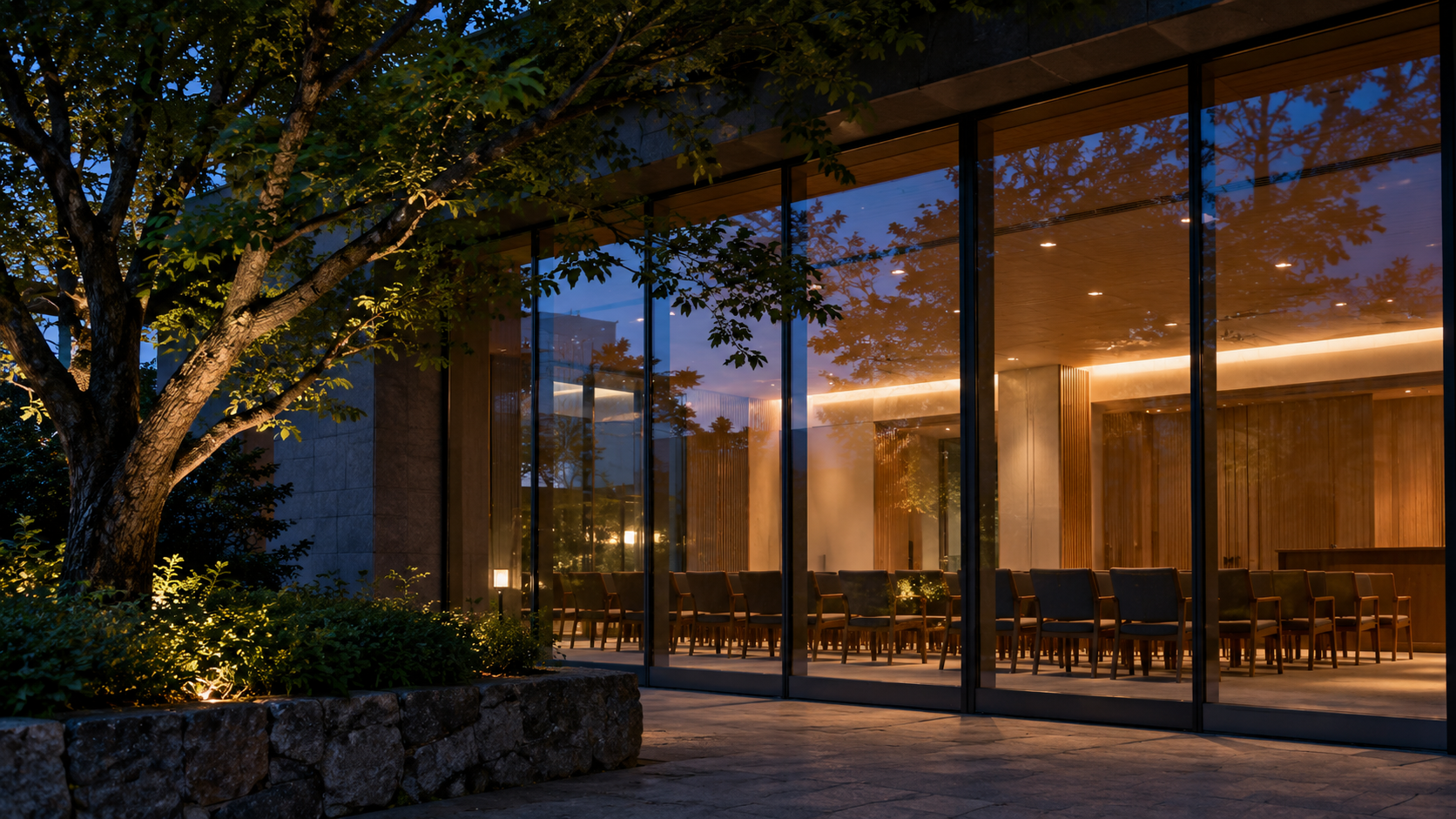 Empty chairs visible through the glass facade of an unbranded civic meeting room at dusk